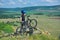 Little child stand next to his mountain bike on mountains edge and looks at the beautiful scenery