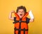 Little child superhero raises arms and shows muscles. Strong confident boy shouts loudly. Kid with broken arm in orange