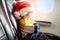 Little child wearing Santa Claus hat traveling by an airplane. Preschooler boy looking at aircraft window during flight. Family