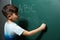 Little child writing letters and doing math on blackboard