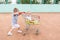 Little children playing at a tennis court with shopping trolley