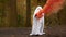 Little children in scary white ghost costume for Halloween is standing in forest holding jack pumpkin smoking with