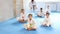 Little children in white kimono sits in a butterfly pose and practices stretching in sport gym