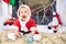 Little Christmas Baby in Santa costume. Child holding Blue Ball near Holiday Lights background.