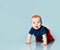 Little chubby child in t-shirt and red shorts. He is creeping on the floor against blue background. Close up, copy space