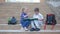 Little classmates with backpacks sitting on steps of school and review the book during break in the fresh air