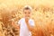 Little country boy eating bread in the wheat field among golden spikes in sun light. Happy rustic life and agriculture concept