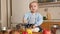 Little crying baby boy trying eating porridge with spoon on kitchen. Concept of healthy nutrition,diet and children food