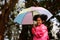 Little curly hair girl wearing raincoat colour pink good humour as she holds a umbrella