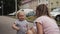 Little curly-haired girl with blue eyes is talking to her mother on the street waving