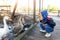 Little cute adorable caucasian curious blond toddler boy in hood sitting near many geese on farm poultry yard enjoy