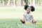 Little cute African kid girl with twin tails hair smiling and sitting on green grass with small white flowers at park