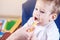 Little cute baby eating on a chair in the kitchen. Mom feeds holding in hand a spoon of porridge