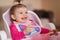 Little cute baby girl are eating in hight chair. Portrait of little smiled child at home