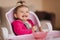 Little cute baby girl are eating in hight chair. Portrait of little smiled child at home