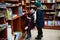 Little cute baby in jacket reaching a book from bookshelf at the library. Learning and education of european kids