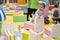 Little cute baby toddler girl in a dress climbs on a carousel in children playcenterDay Care Play Room, soft focus