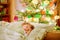 Little cute blond boy sleeping under Christmas tree and dreaming of Santa at home, indoors. Traditional Christian