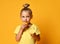 Little cute blond girl in yellow t-shirt holding and licking half of fresh ripe lemon fruit over yellow background