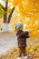 Little cute boy in an autumn coat and cap plays in an autumn park with yellow leaves