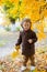 Little cute boy in an autumn coat and cap plays in an autumn park with yellow leaves