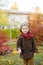 Little cute boy in an autumn coat and cap plays in an autumn park with yellow leaves