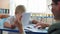 Little cute boy with down syndrome studying mathematics with her female teacher sitting at desk in classroom at