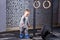 Little cute boy in the grey sportwera standing near barbell against brick wall in the cross fit gym.