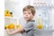 Little cute boy holding banana near open fridge