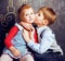 Little cute boy kissing blonde girl in classroom at blackboard, first school love, lifestyle people concept