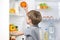 Little cute boy picking orange from fridge