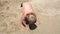 Little cute boy sitting on the sand by the sea in the sun in the summer.