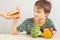 Little cute boy at the table refuses hamburger in favor of fruit and vegetables on white background