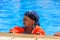 A little cute boy wearing blue bondana and red inflatable armbands learns to swim in the pool.