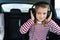 Little cute caucasian girl is driving in car.Kid listening to music with big headphones.Traveling,riding on road in safe baby seat