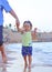 A little cute Caucasian girl in a yellow summer T-shirt is walking with her father`s hand on the sea coast where there is water,