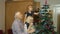 Little cute child girl with senior grandparents family decorating artificial Christmas tree at home