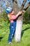 A little cute girl in a cap and jumpsuit in a green garden hugs a tree. nature