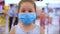 Little Cute Girl from an Epidemic of Coronaviruses or Viruses looks at the Camera Amid Masked People from the Virus who