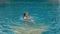 The little cute girl have fun in the pool. The child enjoy summer vacation in a swimming pool jumping, spinning, splash