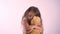 Little cute girl hugging her plush teddy bear and standing isolated on pink studio background