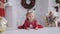 Little cute girl in a red dress smiling lies on the floor in the room with Christmas decor.