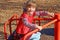 Little cute girl in red vest sits and rides on carousel