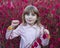 A little cute girl shows a clenched fist, a victory sign against the background of autumn leaves in the Park. Looking at the