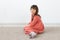 Little cute girl sitting with a modest long pink dress against a white wall. The concept of small innocent children.