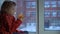 Little cute girl sitting on the window sill, looking out on a snowy cityscape.