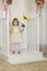 Little cute girl with a sunflower is standing near the door