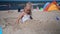 Little cute girl in swimsuit bury cover her body with beach sand. Blurred people