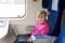 Little cute girl travelling by train. Kid watching movie through laptop with headphones. Children activity and entertainment durin