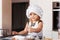 A little cute girl in a white chef hat prepares buns in the kitchen
